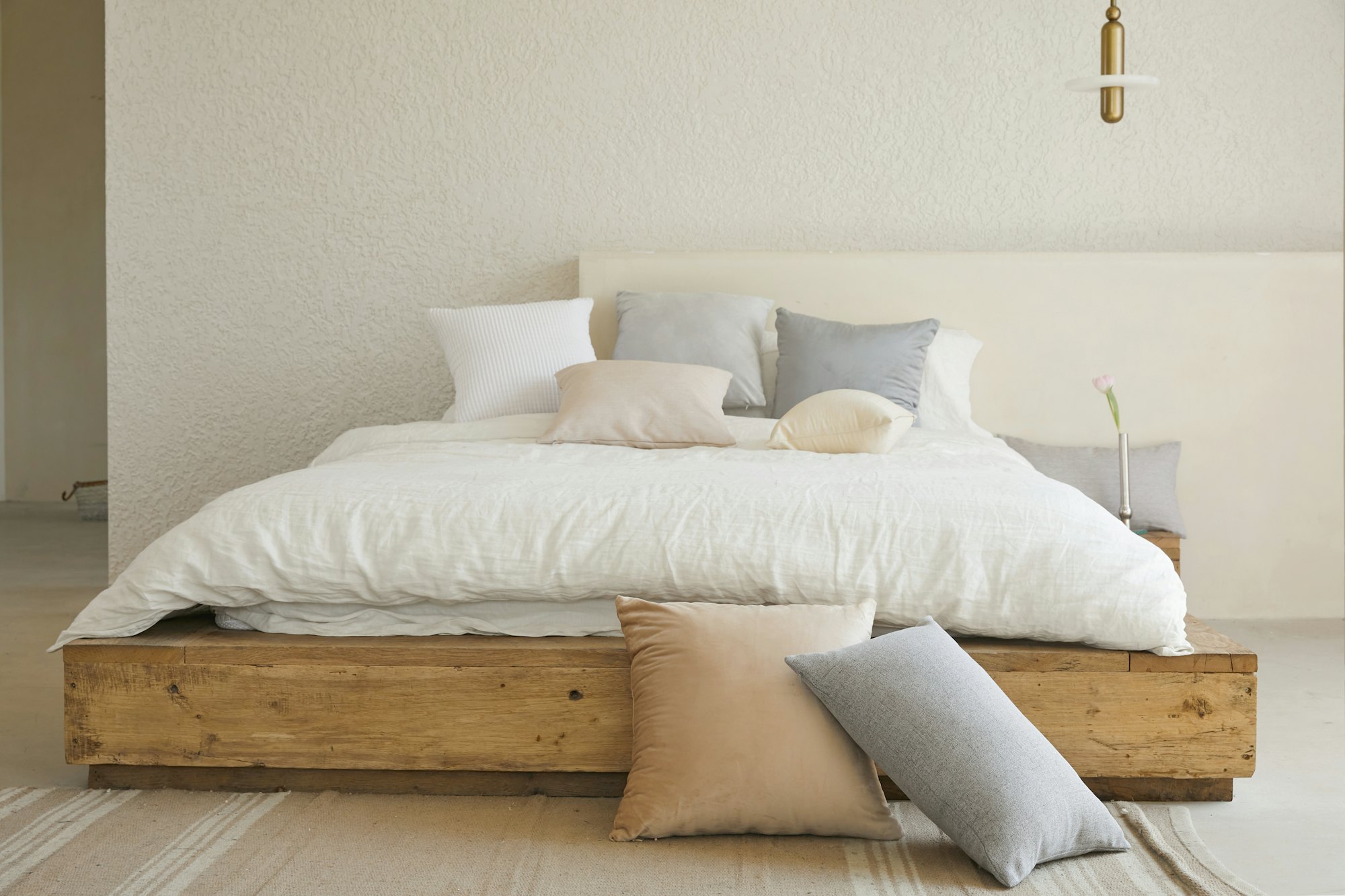 A calm bedroom at Kayana House with soft white linen, a reclaimed-wood bed base and warm morning light