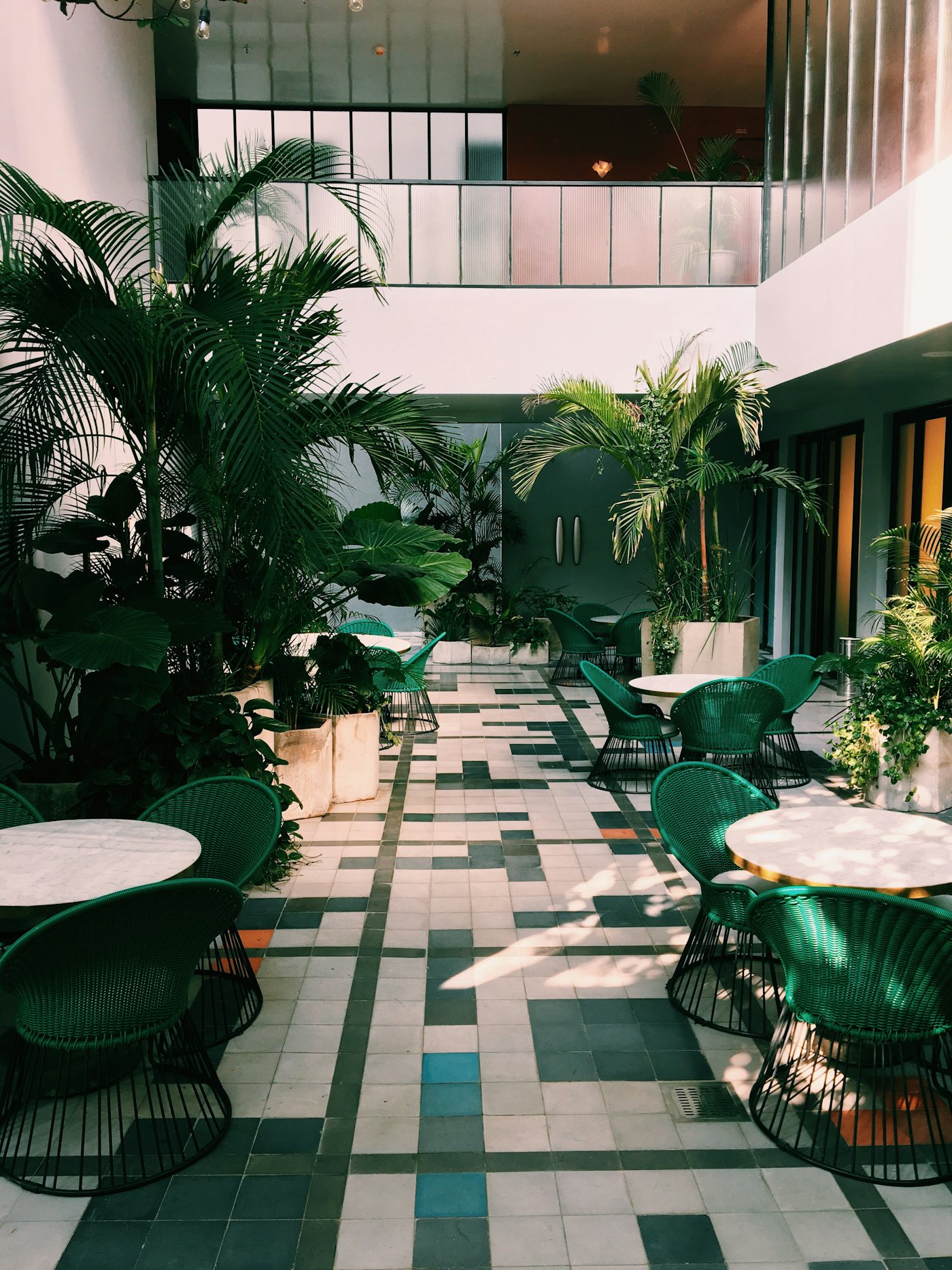 A plant-filled, sunlit communal courtyard with rattan chairs and marble tables at Kayana House